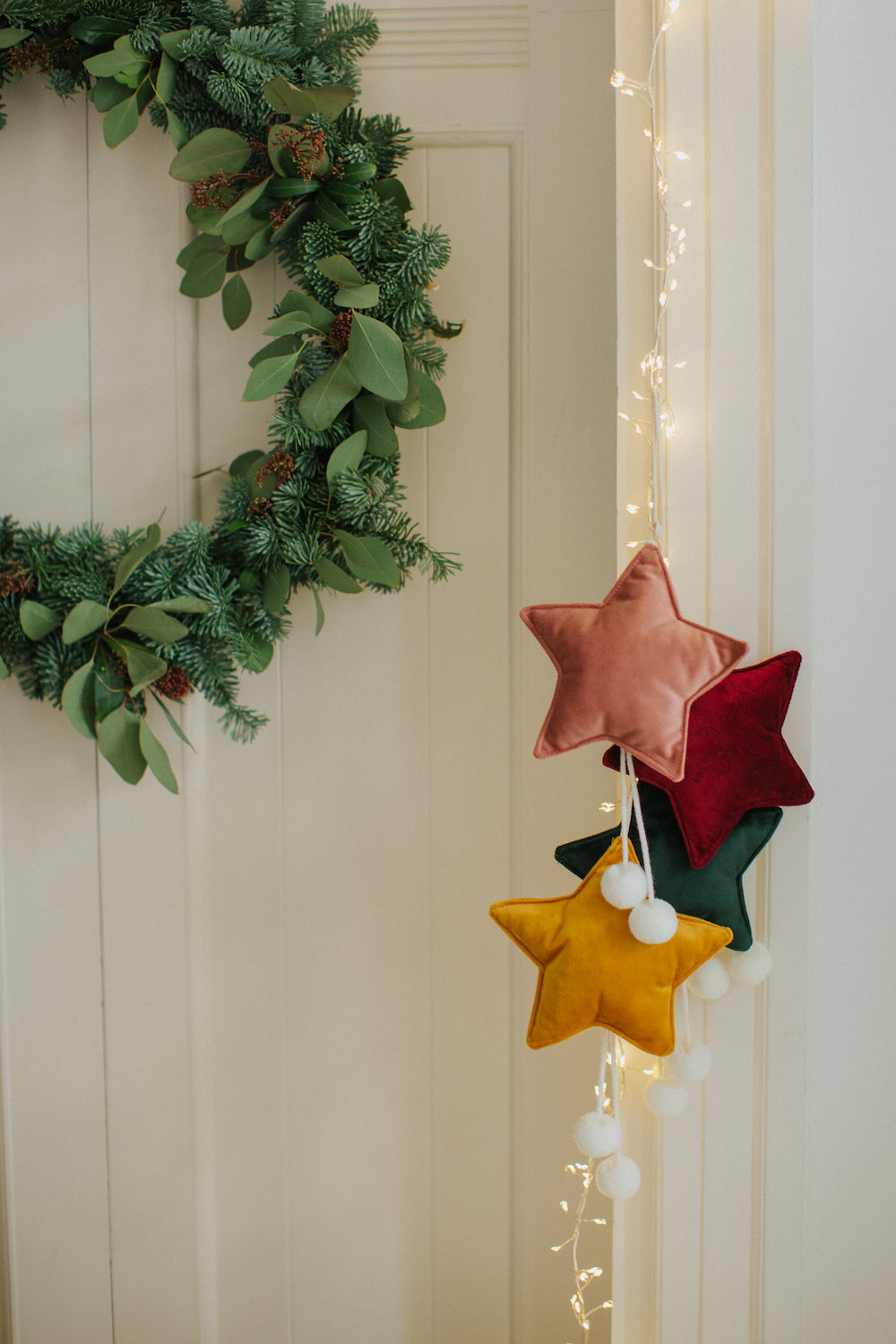 małe zawieszki gwiazdki welurowe wiszące na futrynie drzwi jako dekoracja świąteczna obok wieńca z gałązek