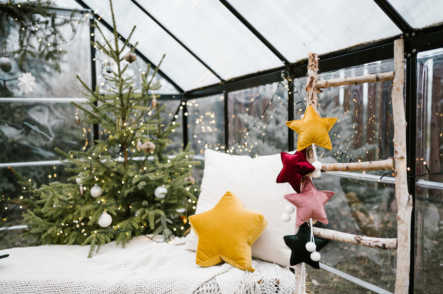 małe zawieszki gwiazdki wiszące w oranżerii obok kanapy i choinki jako ozdoba świąteczna 