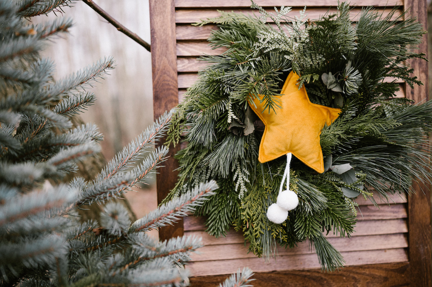mała zawieszka gwiazdka z pomponami w kolorze żółtym od Bettys Home wisząca na wianuszku z igliwia.dekoracja świąteczna 