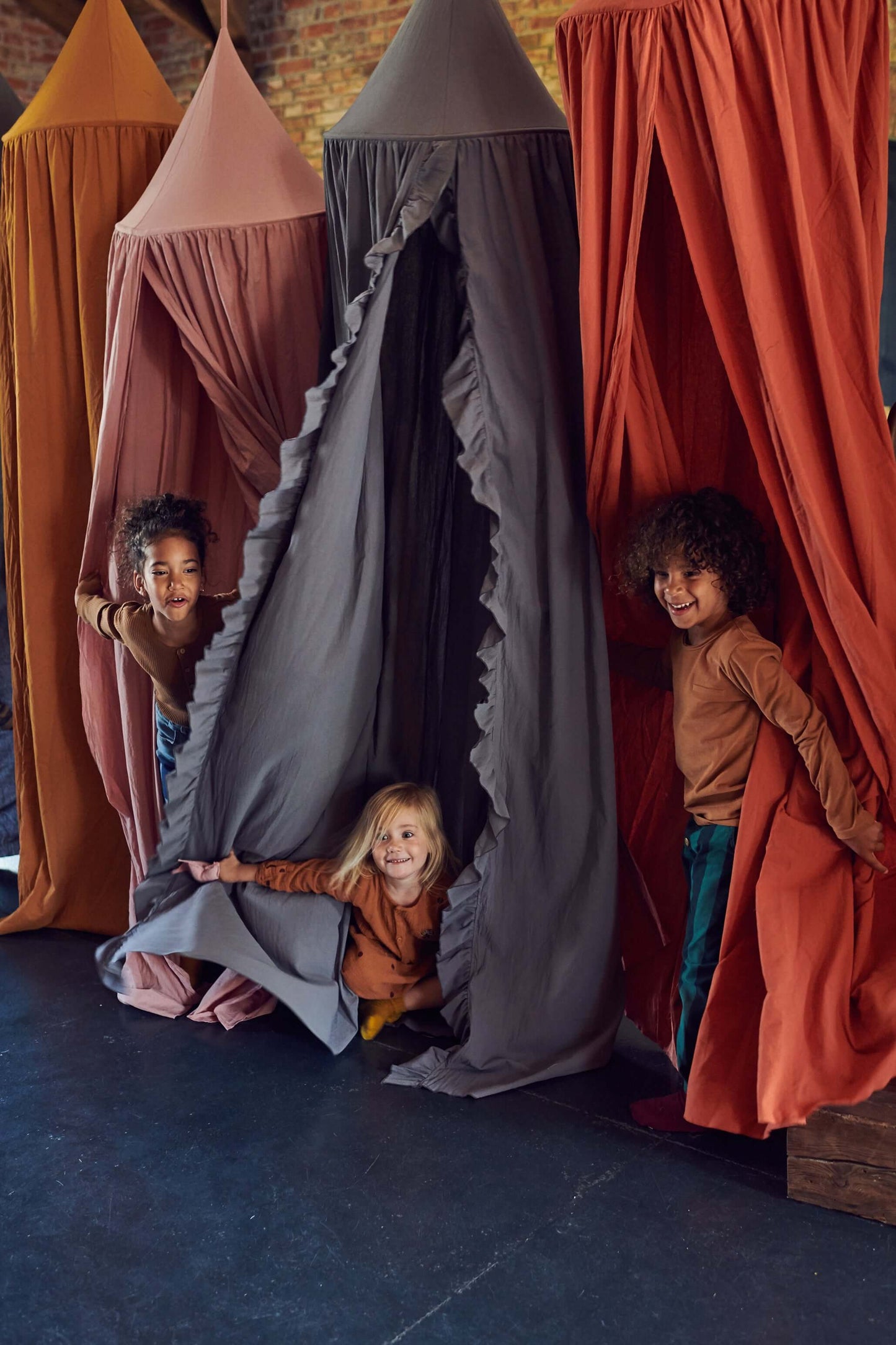 Dzieci się bawią w chowanego w baldachach w trzech róznych kolorach.